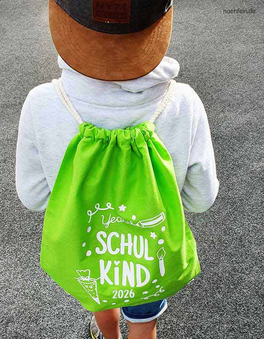 Schulkind 2026 traegt einen Turnbutel - Schultuete und Schriftzug Schulkind 2026- gruner Schulkind Turnbeutel