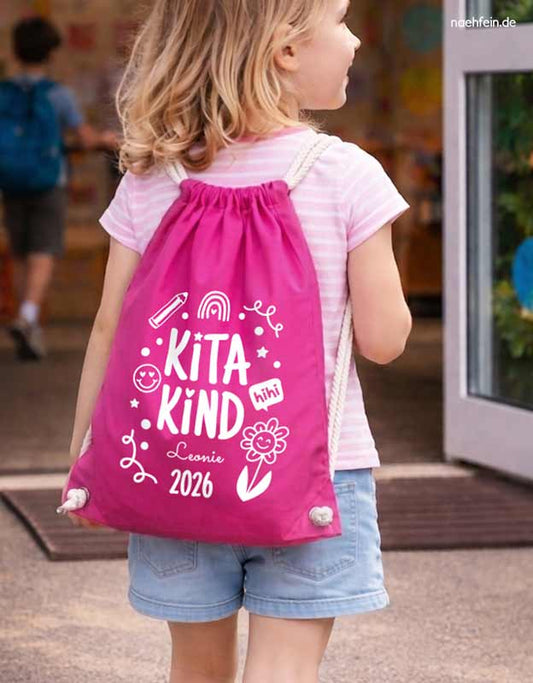 Maedchen vor dem Kindergarten traegt einen pinken Turnbeutel Kitakind 2026 mit Namen - Geschenk Kindergarten - Bilddarstellung KI-generiert